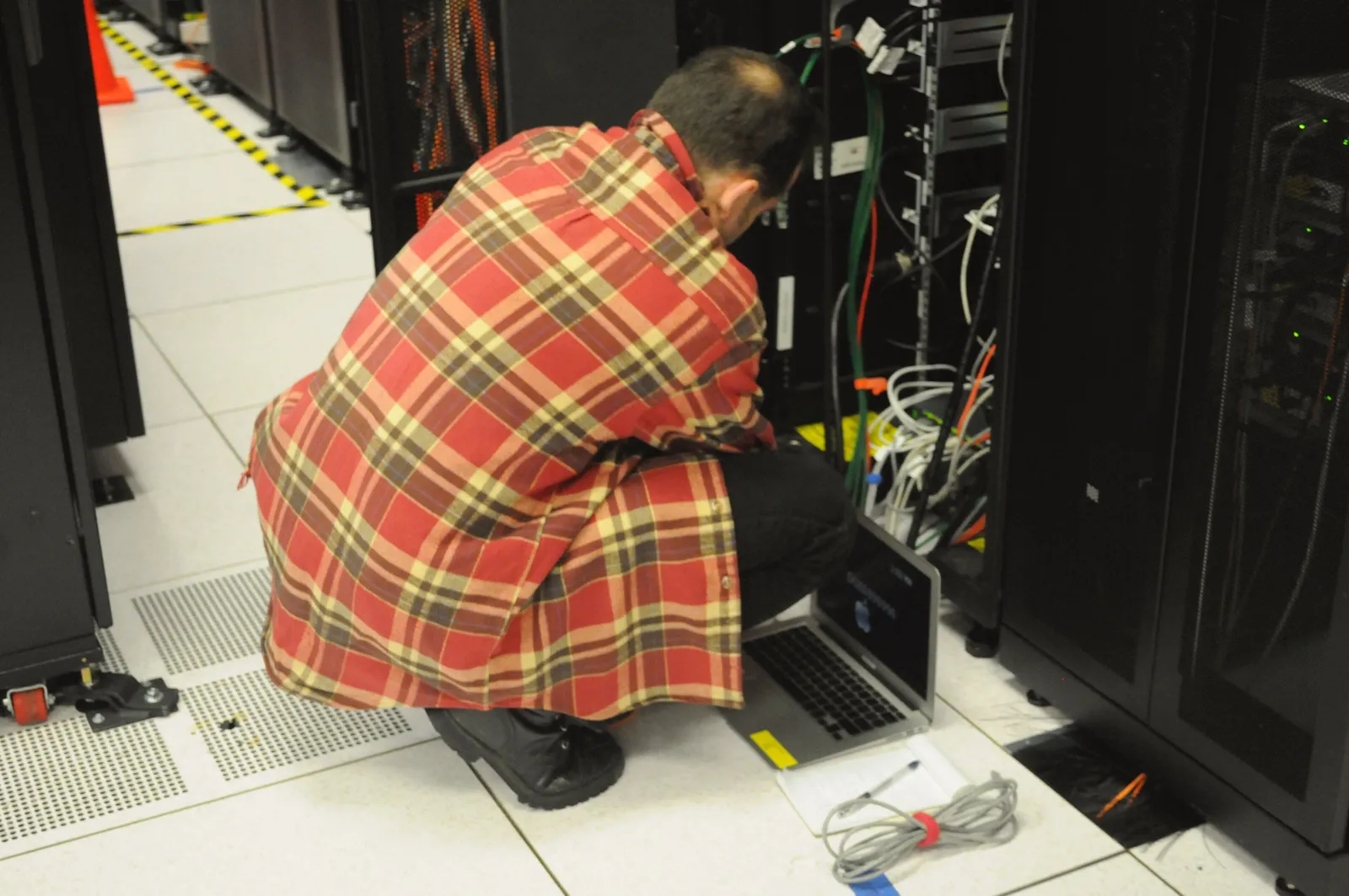 Técnico trabalhando com um laptop em um rack de servidores